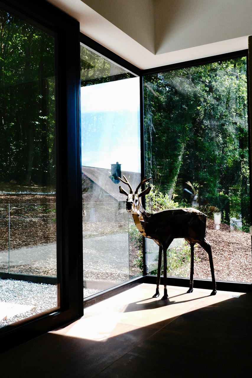 Sculpture de cerf en métal devant les baies vitrées sur les bois au gîte Cit'Art